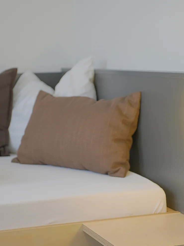 Modernes Bett mit weißen und braunen Kissen neben leuchtender Wandleuchte