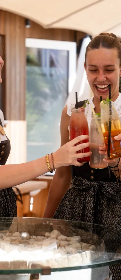 Frauen in Dirndl stoßen im Freien mit bunten Sommergetränken an