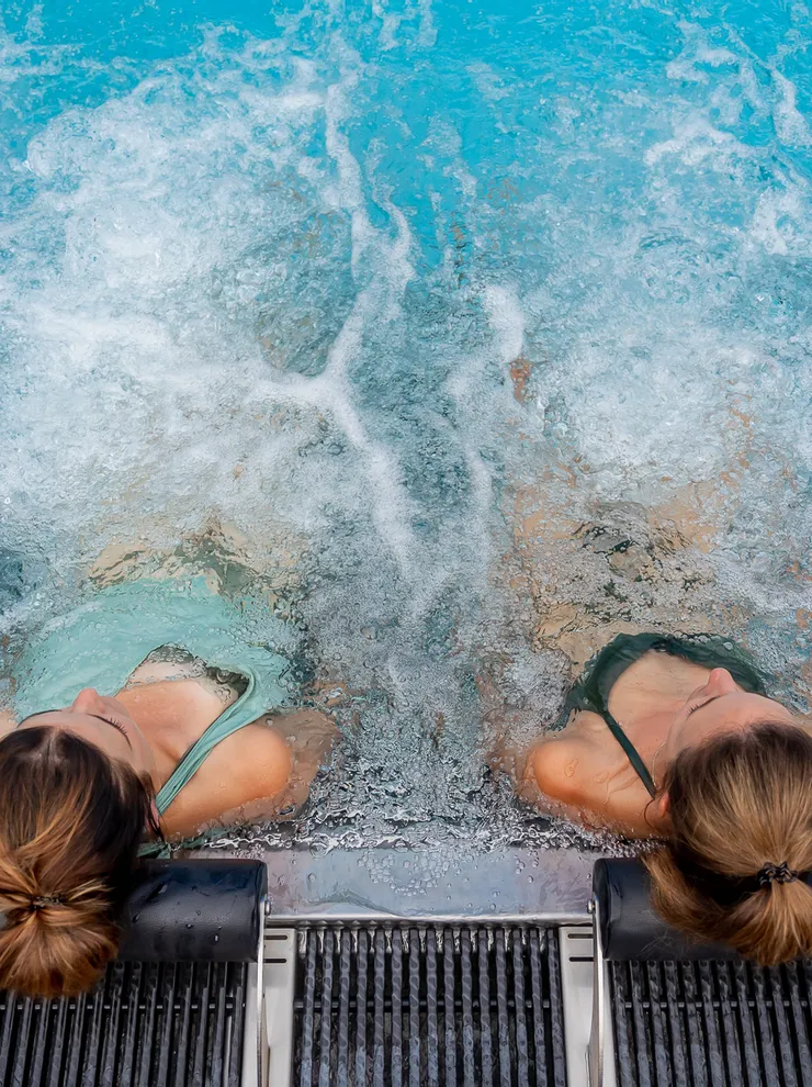 Two women relaxing on pool loungers in bubbling jacuzzi water at a spa