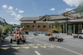 Children riding pedal go-karts on a mini road course at a playground with mountain backdrop