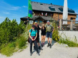 Gruppe von Wanderern vor einer Berghütte bei sonnigem Wetter