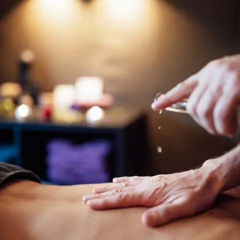 Massageöl wird auf Rücken in entspannter Spa-Atmosphäre aufgetragen