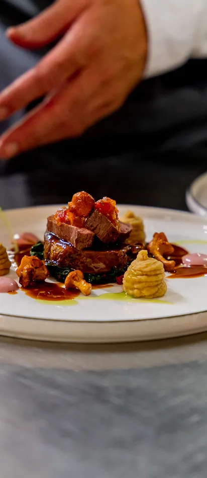 Chef plating gourmet beef dish with artistic sauce and puree decoration