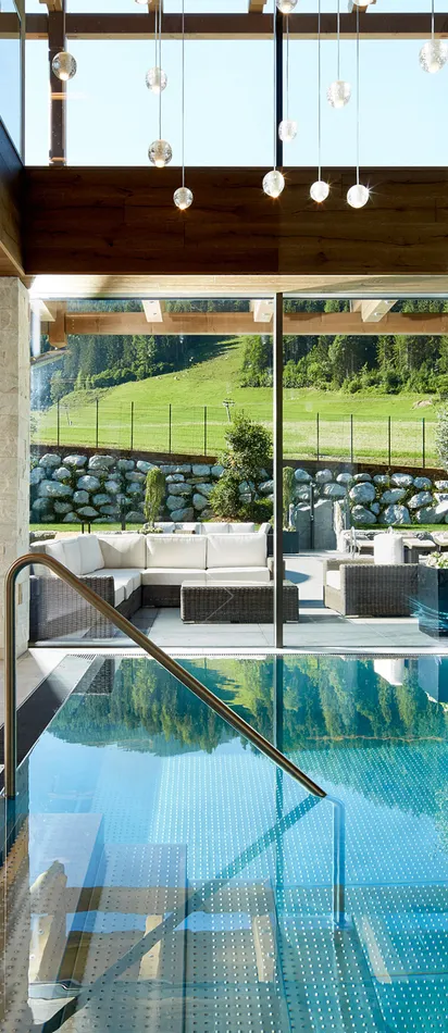 Luxury indoor pool with sun loungers and panoramic view of green alpine landscape