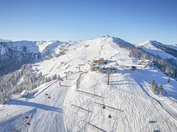 Sonniges Alpenskigebiet mit Sesselliften, verschneiten Pisten und Berghütten