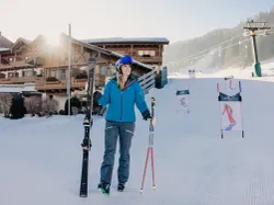 Lächelnde Frau in Skibekleidung mit Skiern und Stöcken an einem verschneiten Skigebiet
