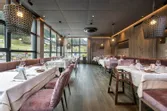 Modernes Restaurant mit großen Fenstern, rosa Samtstühlen und ordentlich gedeckten Tischen