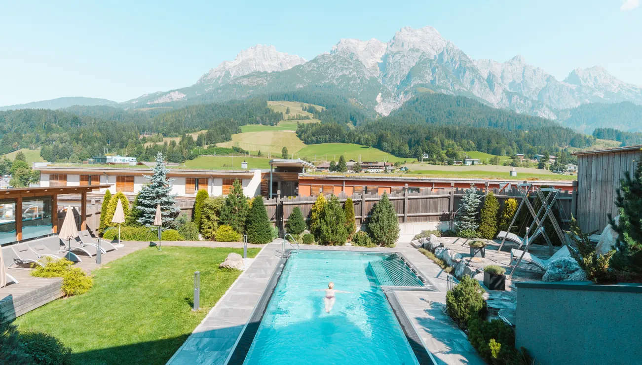 Outdoor swimming pool with sun loungers at hotel resort overlooking alpine mountains