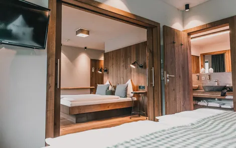 Modern hotel room with wooden decor, double bed, and open bathroom view