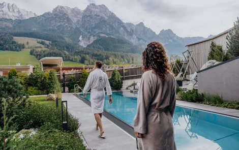 Couple in bathrobes walking by outdoor spa pool with Alpine mountain view