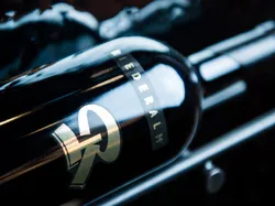 Dunkle Weinflasche mit Riederalm-Etikett in elegantem Weinregal mit Spiegelungen