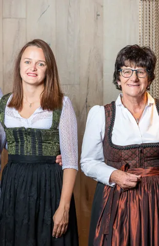 Group portrait of four adults in traditional Austrian attire, standing indoors and smiling at camera