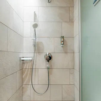 Modern tiled shower with rain shower head and handheld shower in bright bathroom