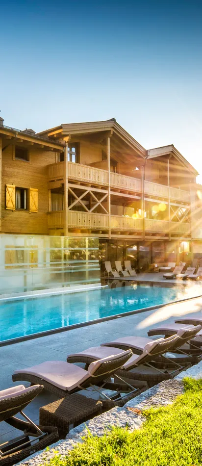 Luxury alpine resort with outdoor pool, sun loungers, and mountain view at sunrise