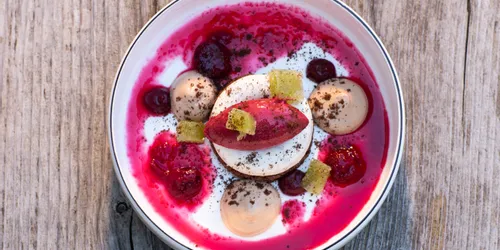 Gourmet-Dessert mit Beerensauce, Mousse und Biskuitwürfeln in weißer Schüssel auf rustikalem Holztisch