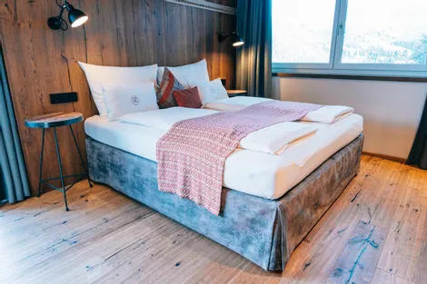 Modern hotel room with double bed, wood panel wall, and large window with mountain view