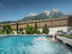 Frau entspannt im Whirlpool mit Blick auf Alpenberge und Holzzaun