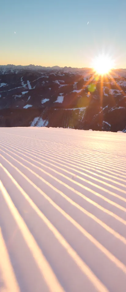 Frisch präparierte Skipiste bei Sonnenaufgang in verschneiter Berglandschaft