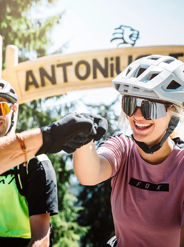 Mountain bikers fist bump at the start of Antonius Trail in forest setting