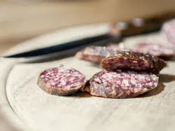 Sliced dry cured salami on a wooden cutting board with knife in background