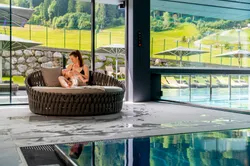 Mutter stillt Baby auf runder Liege neben Innenpool mit Bergblick