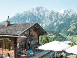 Mountain hut restaurant with outdoor seating overlooking alpine valley and rugged peaks