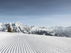 Freshly groomed ski slope with snow-covered Alps under clear blue sky