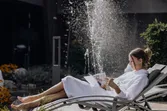 Frau entspannt auf Liegestuhl im Spa-Garten mit Magazin neben Wasserspiel