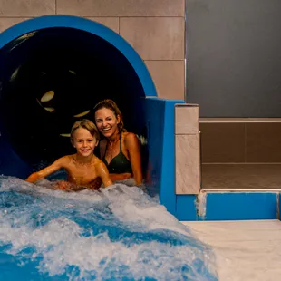 Lächelnde Mutter und Sohn kommen aus der Indoor-Wasserrutsche ins Becken