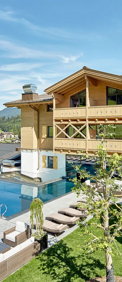 Family hotel with outdoor pool, sun loungers, and water slide in alpine mountain setting