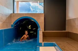 Lächelnder Junge verlässt Indoor-Wasserrutsche in flaches blaues Becken im Wasserpark