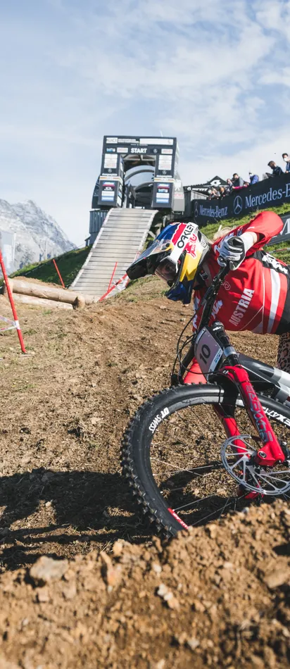 Downhill mountain biker in Austria jersey racing around dirt turn on mountain trail