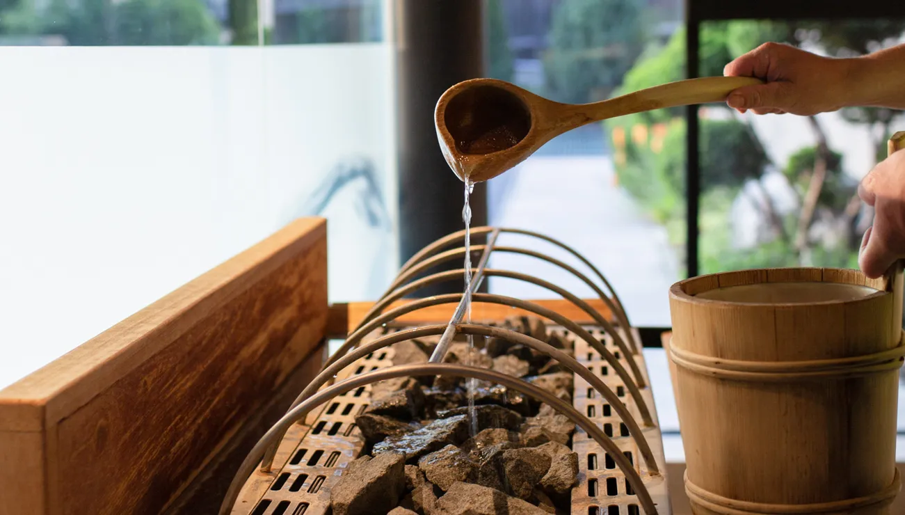 Wasser wird mit Holzschöpfkelle auf heiße Saunasteine in modernem Spa gegossen
