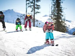 Children learning to ski on a sunny snow-covered slope wearing helmets and ski gear