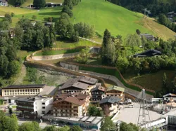 Alpendorf mit Hotels und Seilbahnstation, umgeben von grünen Hügeln und Wald