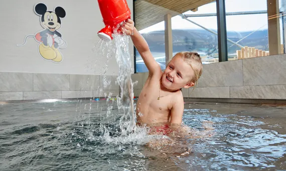 Lächelndes Kind spielt mit roter Gießkanne im Indoor-Kinderbecken
