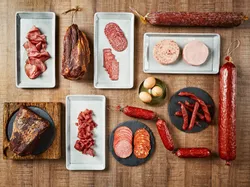 Assorted deli meats and sausages on plates and boards on a wooden table