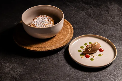 Chocolate mousse with nuts and berry sauce next to a powdered soufflé in a ceramic bowl
