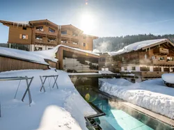 Luxury alpine hotel with outdoor heated pool surrounded by snow in winter sunlight