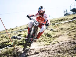 Downhill-Mountainbiker fährt mit roter Ausrüstung und GoPro-Helm über felsigen Trail