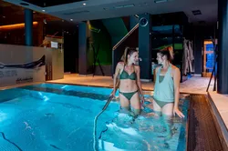 Zwei Frauen in Badekleidung entspannen lächelnd im luxuriösen Indoor-Spa-Pool