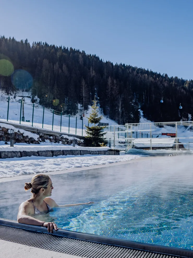 Frau entspannt in beheiztem Außenpool mit Blick auf verschneite Alpen