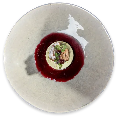 Gourmet dessert with green mousse, red berry sauce and edible garnish on ceramic plate