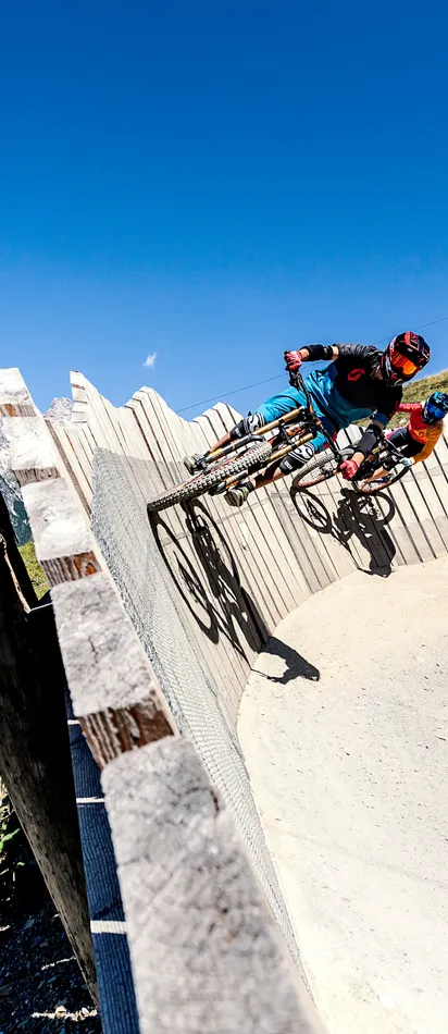 Mountainbiker fahren auf steiler Holzkurve im alpinen Bikepark mit Bergpanorama