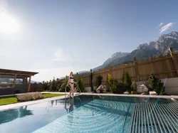 Frau im Bikini steigt in Außenpool eines Luxushotels mit Bergblick
