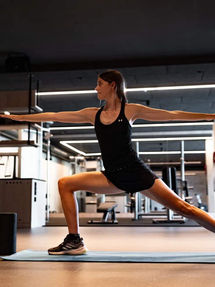 Frau macht Krieger-Yoga-Pose auf Matte im modernen Fitnessstudio