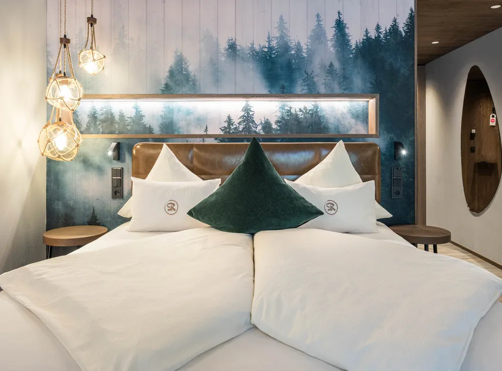 Modern hotel room with double bed, forest wall mural and rope pendant lights
