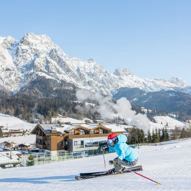 Skifahrer zieht Schwung auf präparierter Piste vor schneebedeckten Alpen und Chalets