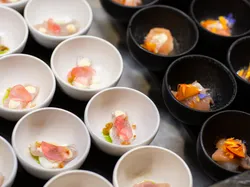 Verschiedene Gourmet-Vorspeisen in weißen und schwarzen Schalen mit rohem Fisch und essbaren Blüten