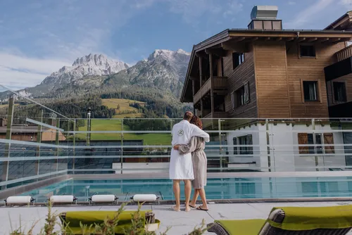 Paar im Bademantel am Pool eines Alpenresorts mit Blick auf die Berge